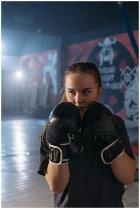 Focused young woman boxer in gym training with glo