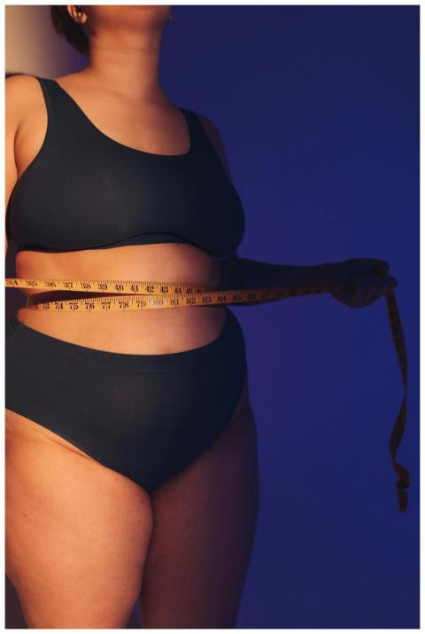 Plus-size woman measuring waist with tape measure
