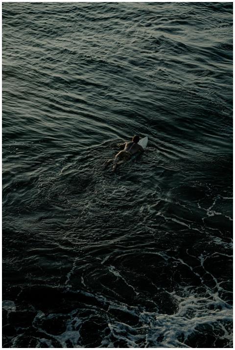 A lone surfer paddles through the dark waves, prep