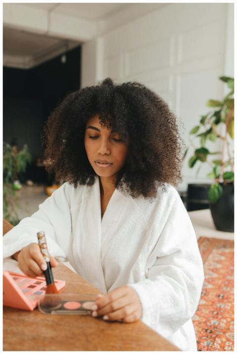 A woman with curly hair in a bathrobe applies make