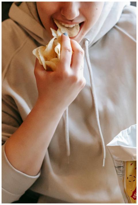 Crop female in comfy hoodie eating tasty savory po