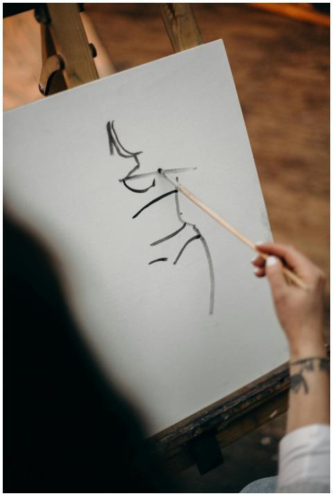Artist's hand sketching a portrait on canvas with
