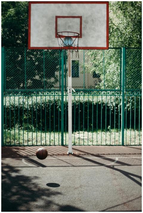 An outdoor basketball hoop with a ball on a sunny