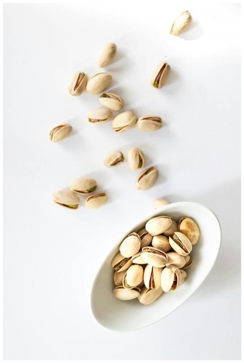 Pistachio nuts in a white bowl on a white backgrou