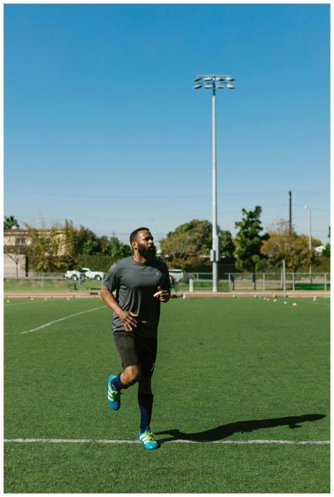 A Black male athlete jogging on a green field, sho