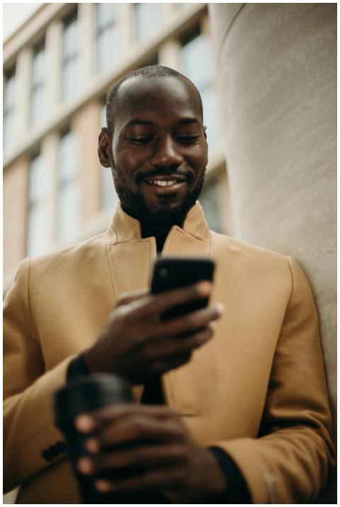 A cheerful man in a stylish coat using his smartph