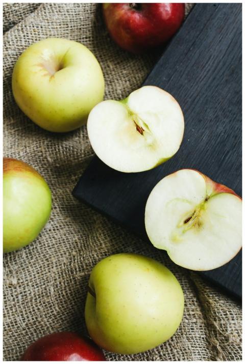 A mix of whole and sliced green and red apples on