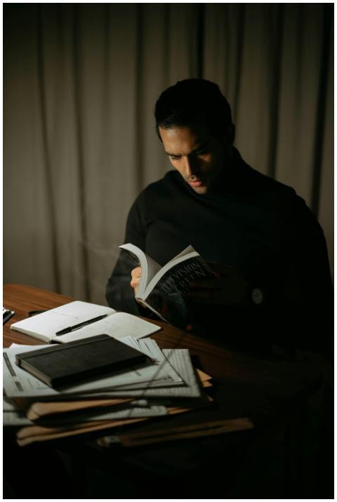 Concentrated male turning pages of book while sitt