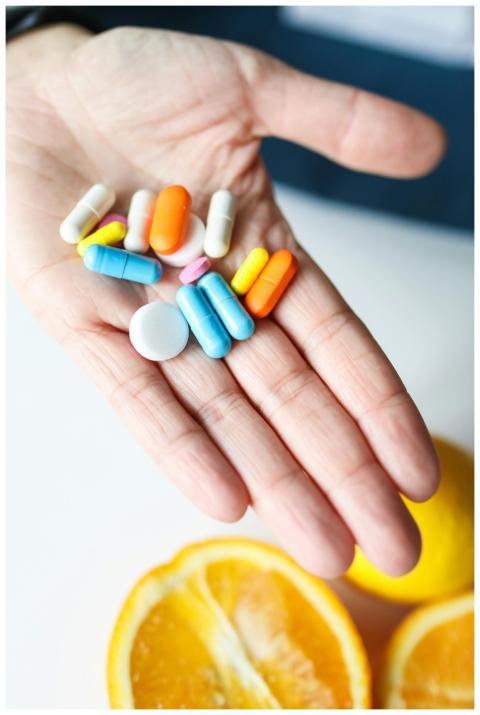 Hand holding colorful pills next to fresh orange s