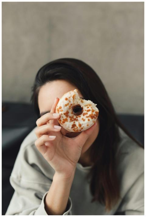 An adult woman in a gray sweater holds a donut in