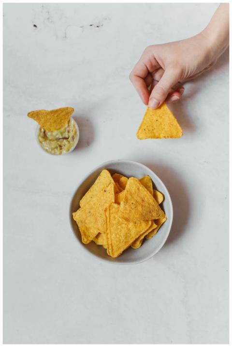 A hand holding a nacho over a bowl with dipping sa