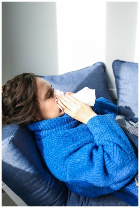 A woman in a blue sweater uses a tissue, lying ind