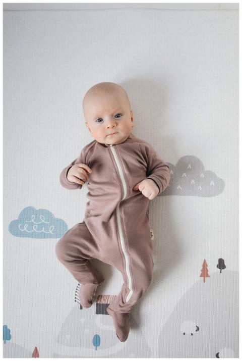 Cute baby in brown onesie lying on a stylish nurse