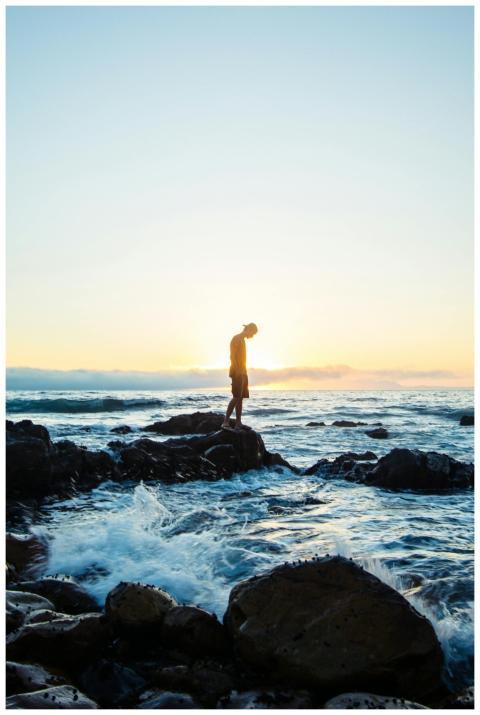 A tranquil scene of a man standing on rocks by the