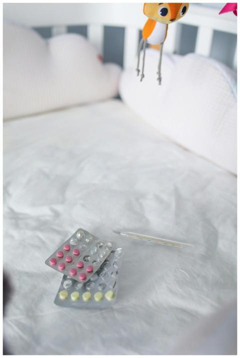 Blister packs and thermometer on a soft crib mattr
