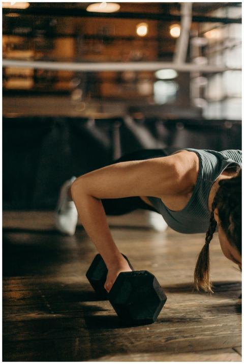 Fit woman doing a dumbbell push-up in a gym, highl