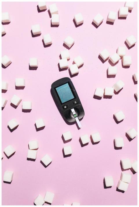 A glucometer on a pink background surrounded by su