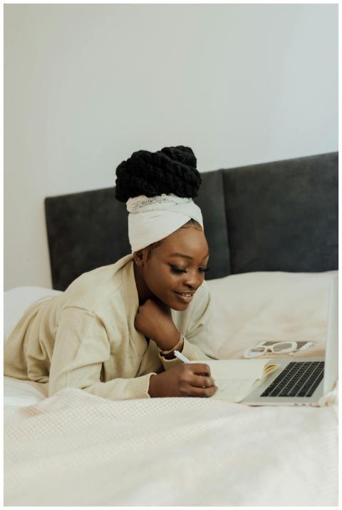 A woman with afro hair works from bed using her la