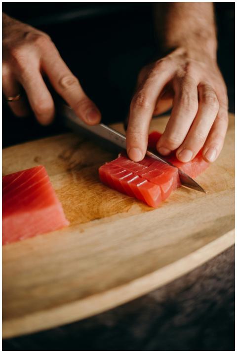 Close-up of hands slicing fresh tuna on a wooden c