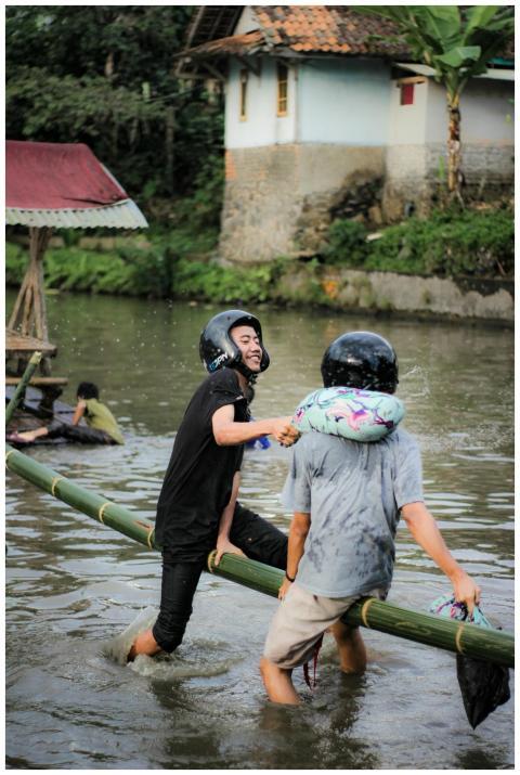 Two young men playing on a bamboo bridge over a ri