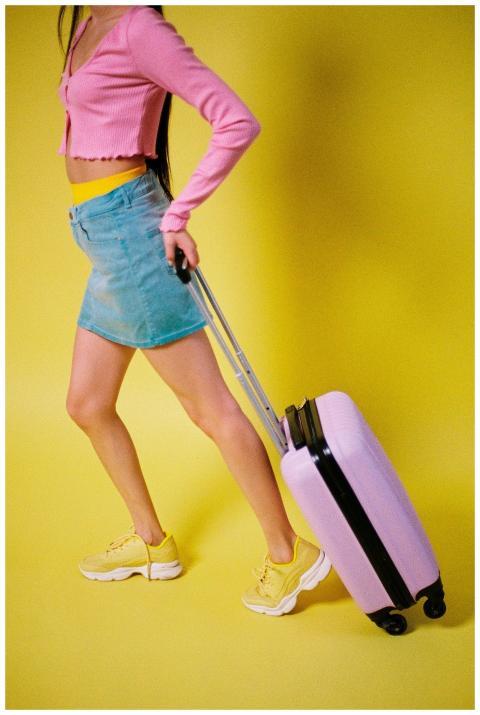 Woman in denim skirt and pink top pulling a suitca