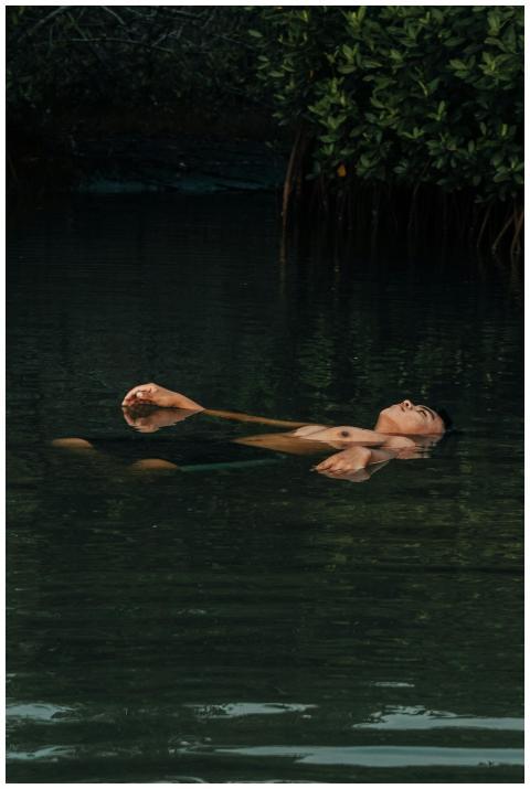 A man peacefully floats on calm water surrounded b