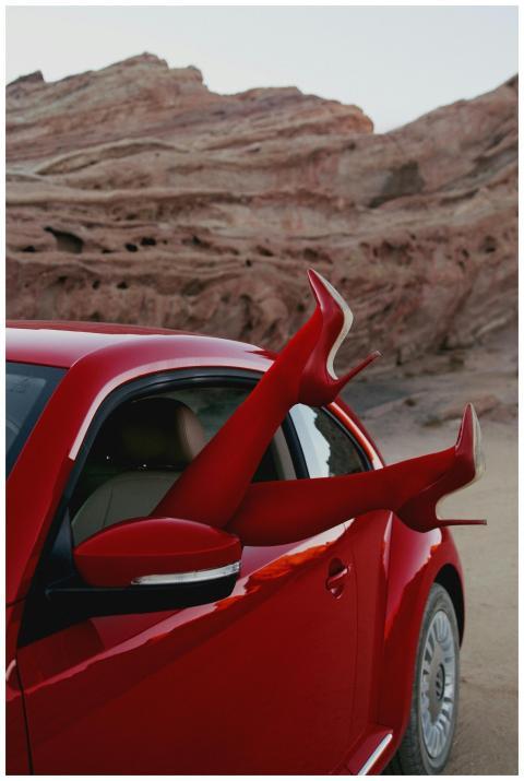 Red sports car with legs in high heels against a d