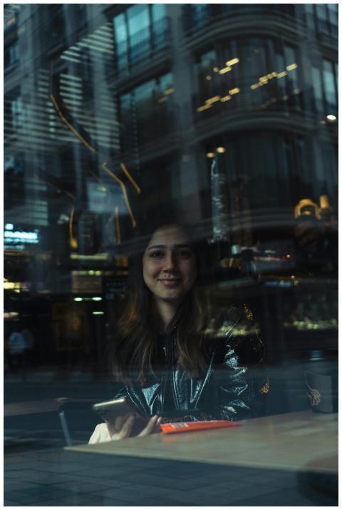 A woman smiles through a glass window with city re