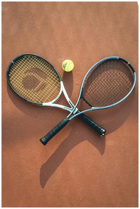 Two tennis rackets and a ball arranged on a clay c