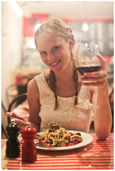 Smiling woman having pasta and wine in a cozy rest