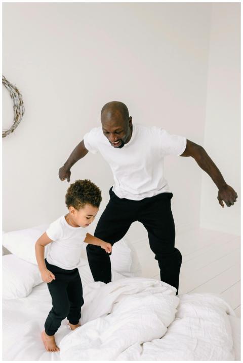 African American father and son jumping on a bed i