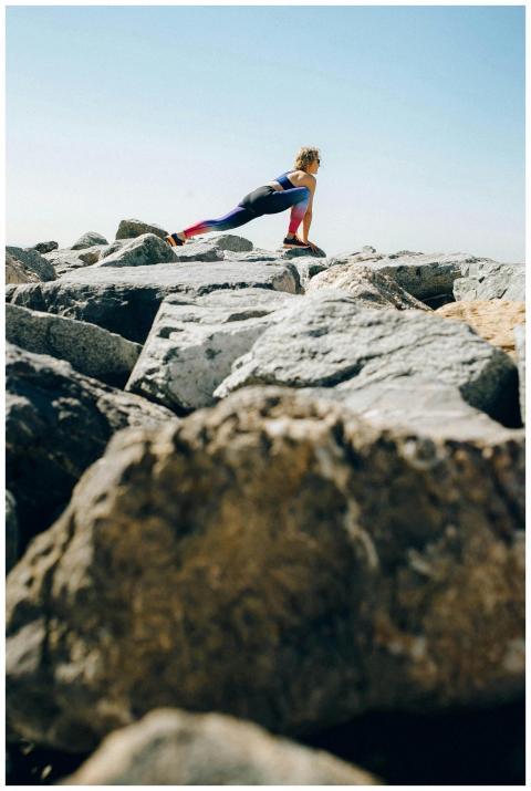 A woman stretches on rocky terrain under a clear s