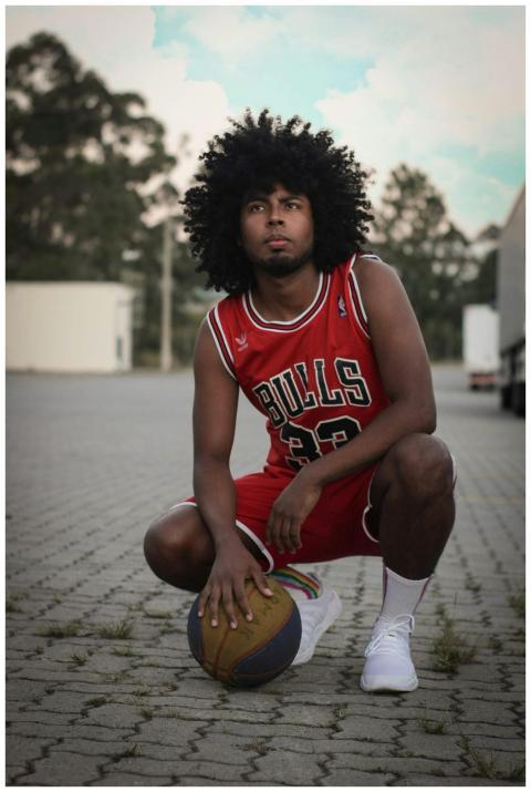 Young man with afro hair in basketball jersey crou