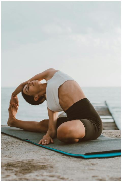 Adult woman practicing yoga on a wooden dock by th