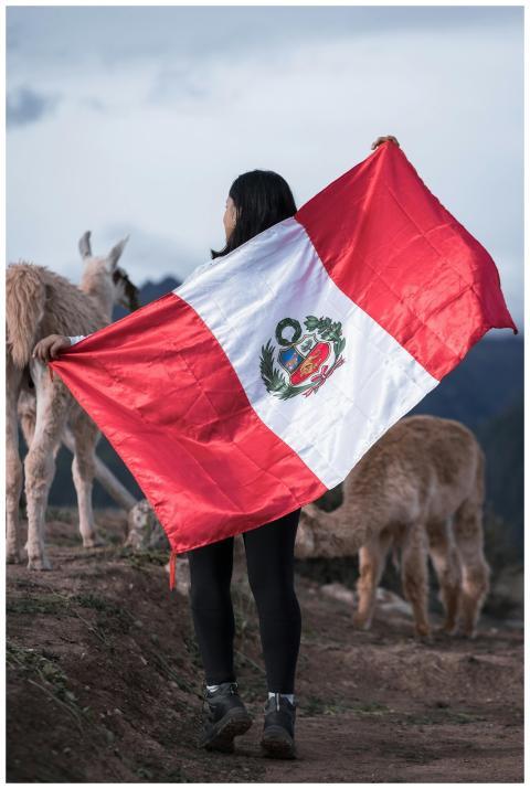 A woman holding the Peruvian flag stands in a rura