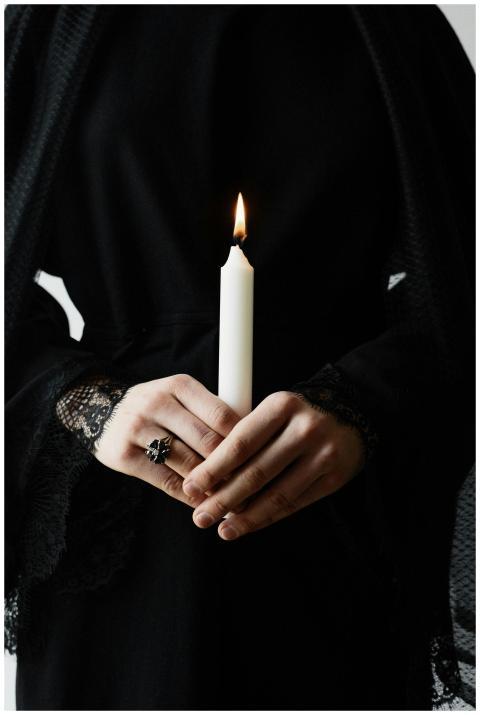 A person in dark clothing holds a burning candle,