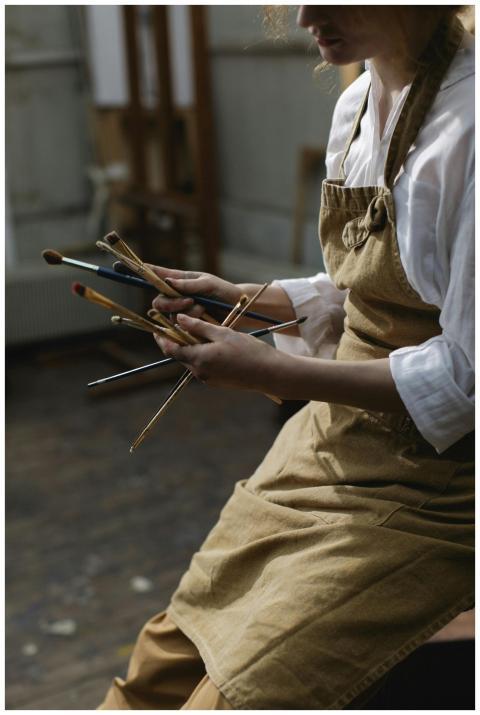Artist with apron holding multiple paintbrushes in