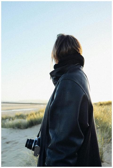 Woman in leather jacket with camera by ocean shore