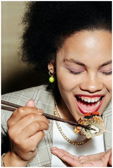 An adult woman with curly hair enjoying sushi whil