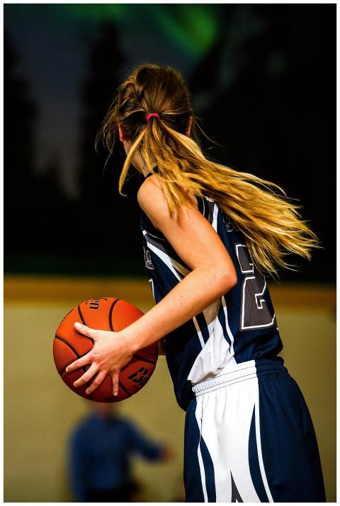 A young female basketball player holding a ball du