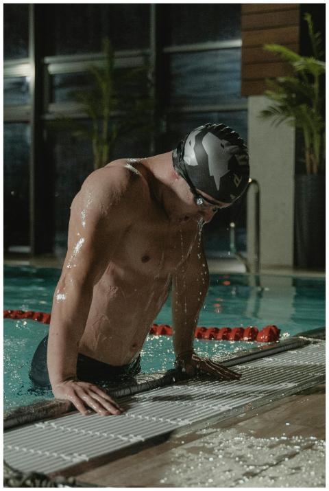 A male athlete in a swim cap exits a swimming pool