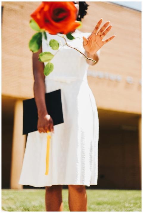 A faceless graduate in a white dress holds a rose