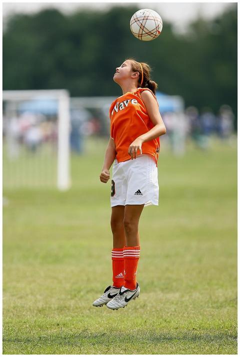 A young girl jumps to head a soccer ball during a