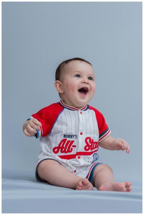 Smiling baby wearing a baseball-themed romper, sit