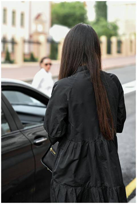 Woman with long hair in black dress by car on a ci