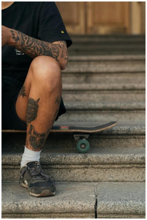 A tattooed skater sits on concrete steps with a lo