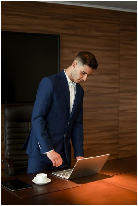 A young businessman in a blue suit works on a lapt