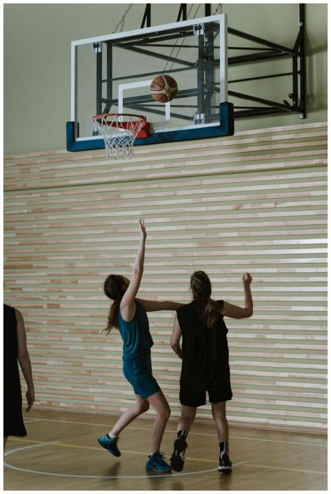 Two women playing basketball indoors, reaching for