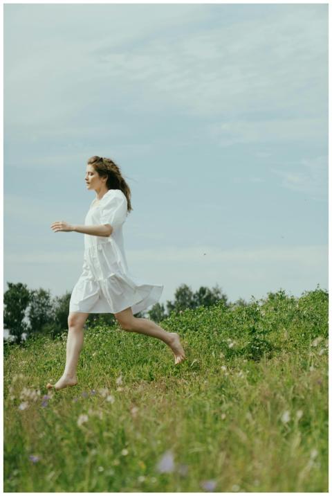A woman in a white dress joyfully runs barefoot ac