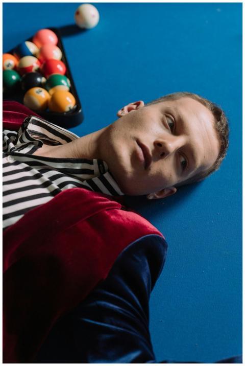 A man in a striped shirt and velvet jacket lying o